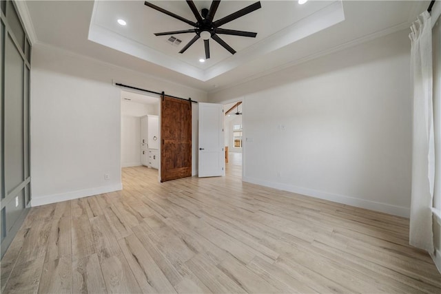 unfurnished bedroom featuring light hardwood / wood-style flooring, a raised ceiling, ceiling fan, a barn door, and ornamental molding