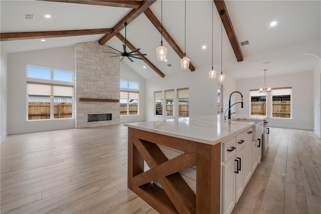 kitchen featuring a large island, hanging light fixtures, light wood-type flooring, a fireplace, and white cabinets