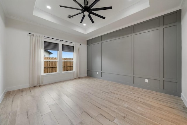 unfurnished room featuring ceiling fan, light wood-type flooring, ornamental molding, and a tray ceiling