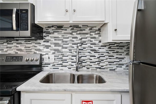 kitchen featuring tasteful backsplash, appliances with stainless steel finishes, light stone countertops, white cabinetry, and a sink