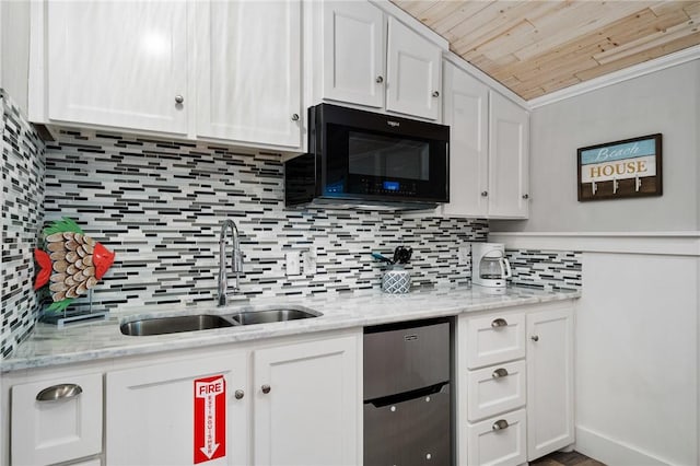 kitchen with white cabinets, light stone counters, a sink, black microwave, and backsplash