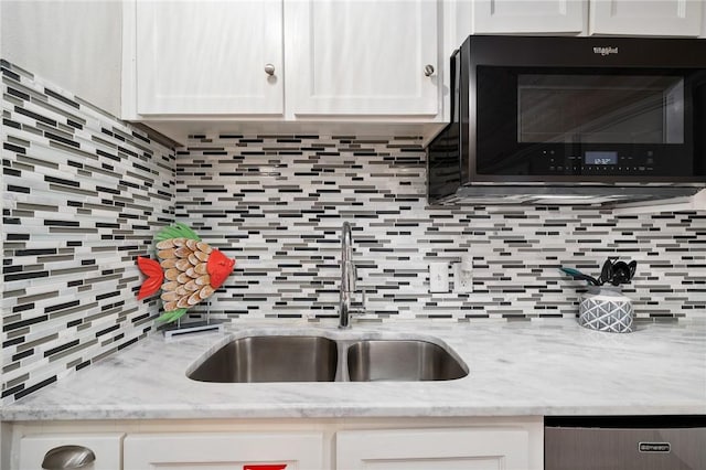 kitchen with light stone counters, white cabinetry, a sink, and decorative backsplash