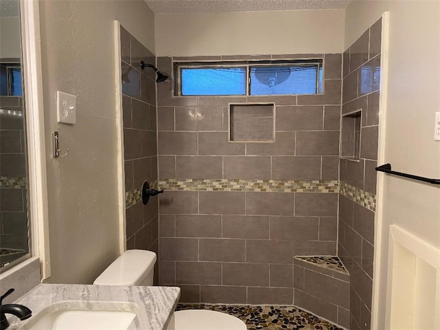 bathroom with vanity, toilet, a textured ceiling, and a tile shower