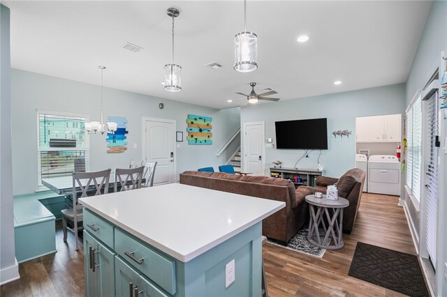 kitchen featuring washing machine and clothes dryer, dark wood-type flooring, a kitchen island, and decorative light fixtures