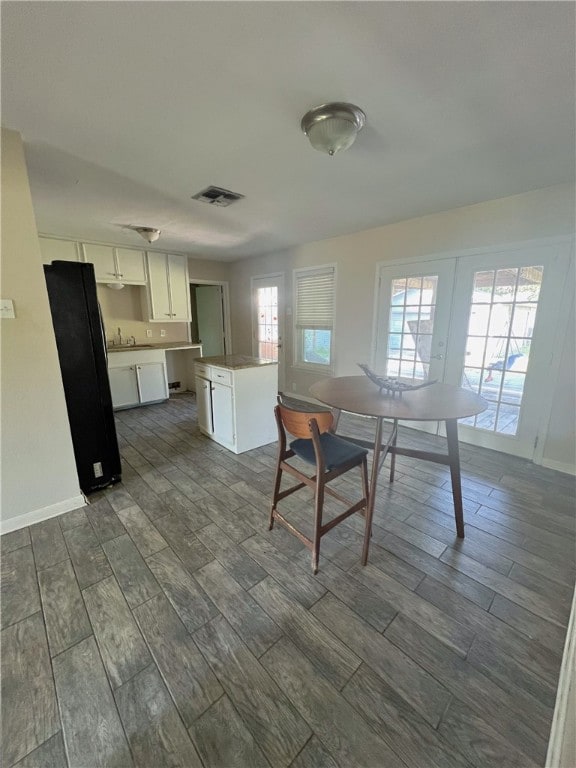 kitchen with black fridge, french doors, white cabinetry, dark wood-type flooring, and a center island