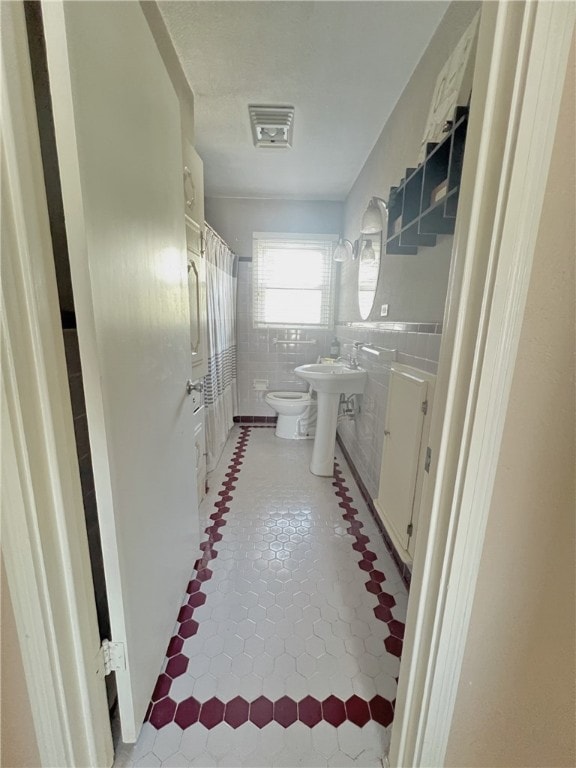 bathroom with toilet, tile walls, a bidet, and tile patterned flooring