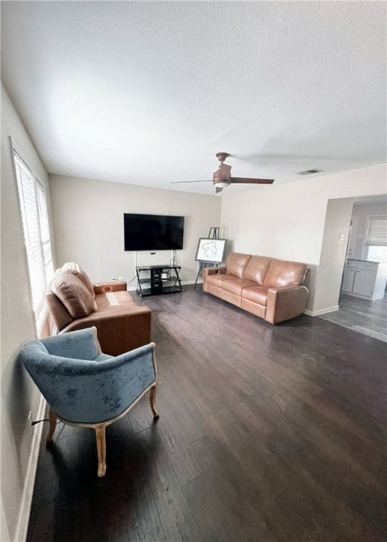 living room featuring dark wood-type flooring, ceiling fan, and a textured ceiling