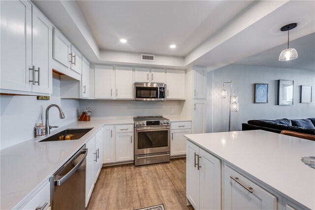 kitchen with light wood-type flooring, white cabinetry, appliances with stainless steel finishes, hanging light fixtures, and sink