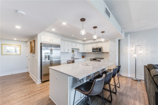 kitchen featuring decorative light fixtures, appliances with stainless steel finishes, a breakfast bar area, and white cabinets