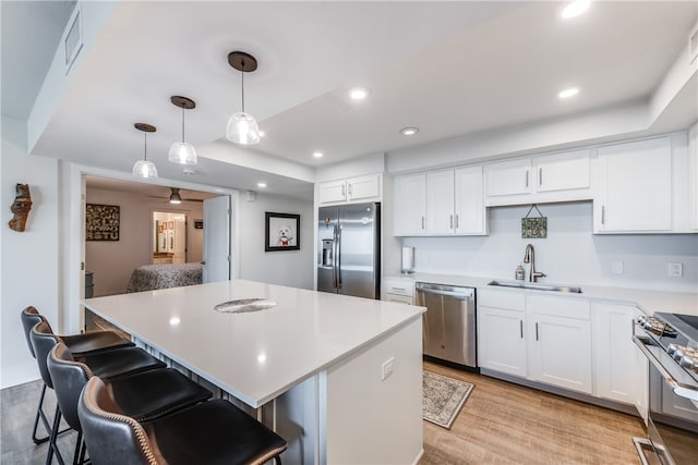 kitchen with stainless steel appliances, a kitchen island, pendant lighting, sink, and light hardwood / wood-style floors