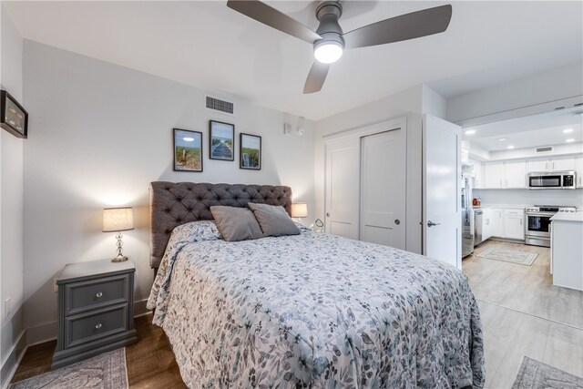 bedroom featuring stainless steel fridge, light hardwood / wood-style floors, ceiling fan, and a closet