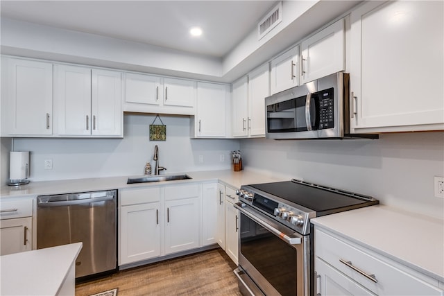 kitchen with stainless steel appliances, white cabinets, sink, and light wood-type flooring