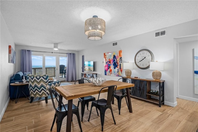 dining area featuring baseboards, light wood-style flooring, visible vents, and a textured ceiling