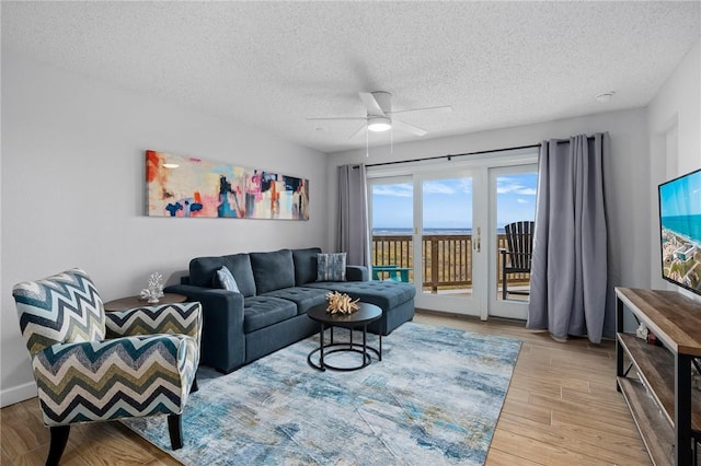 living area with light wood-style floors, ceiling fan, and a textured ceiling