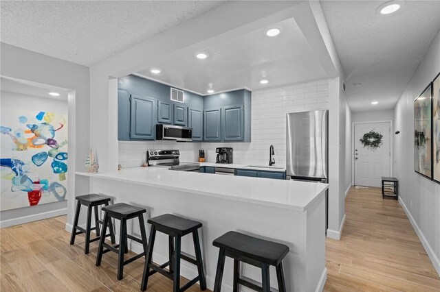 kitchen with stainless steel appliances, blue cabinets, a peninsula, a kitchen bar, and a sink