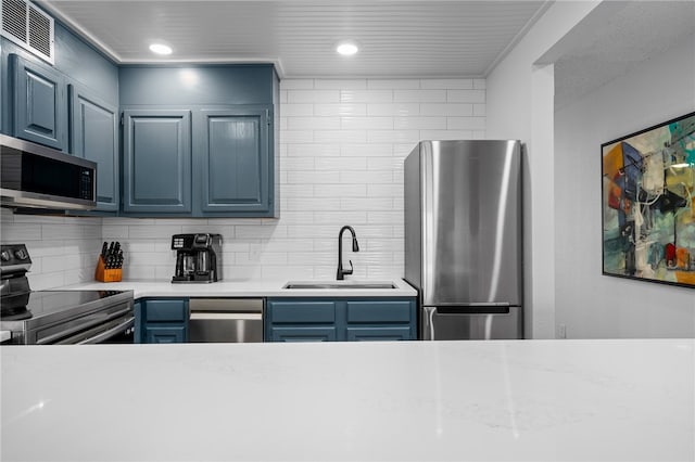 kitchen with blue cabinets, appliances with stainless steel finishes, backsplash, and a sink