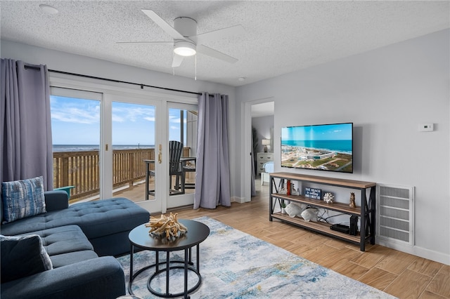 living area with a textured ceiling, ceiling fan, wood finish floors, visible vents, and baseboards