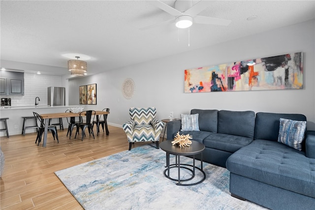 living room featuring ceiling fan, light wood finished floors, a textured ceiling, and baseboards