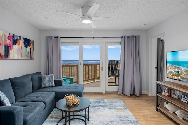 living room featuring a ceiling fan, baseboards, a textured ceiling, and light wood finished floors