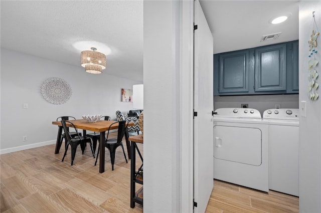 clothes washing area with washing machine and clothes dryer, cabinet space, visible vents, wood tiled floor, and baseboards