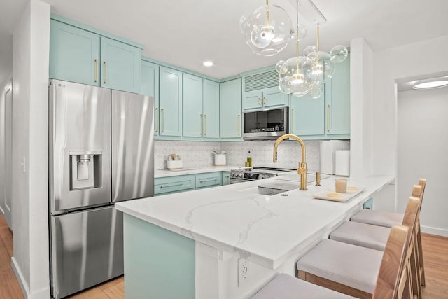 kitchen with light stone countertops, hanging light fixtures, stainless steel appliances, backsplash, and light hardwood / wood-style floors