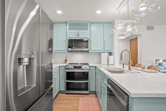 kitchen featuring decorative backsplash, appliances with stainless steel finishes, sink, light hardwood / wood-style flooring, and hanging light fixtures