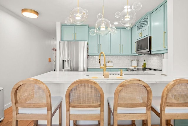 kitchen featuring a breakfast bar, appliances with stainless steel finishes, tasteful backsplash, decorative light fixtures, and kitchen peninsula