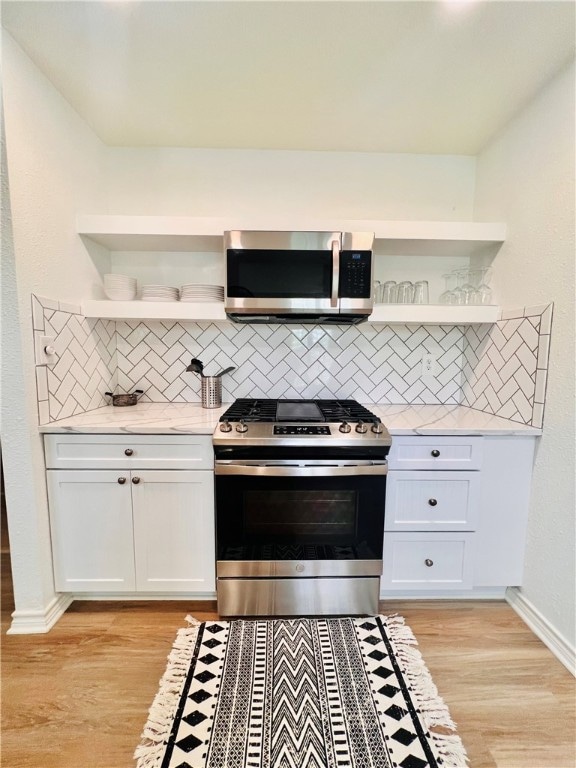 kitchen with white cabinets, light wood-type flooring, appliances with stainless steel finishes, and backsplash