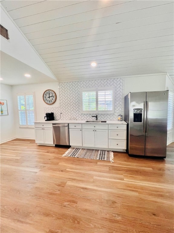 kitchen with light hardwood / wood-style floors, lofted ceiling, white cabinets, backsplash, and appliances with stainless steel finishes