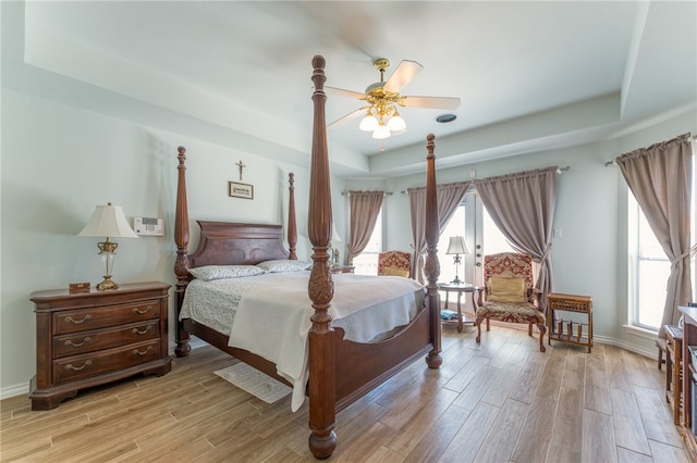 bedroom featuring ceiling fan, multiple windows, light wood-type flooring, and a tray ceiling