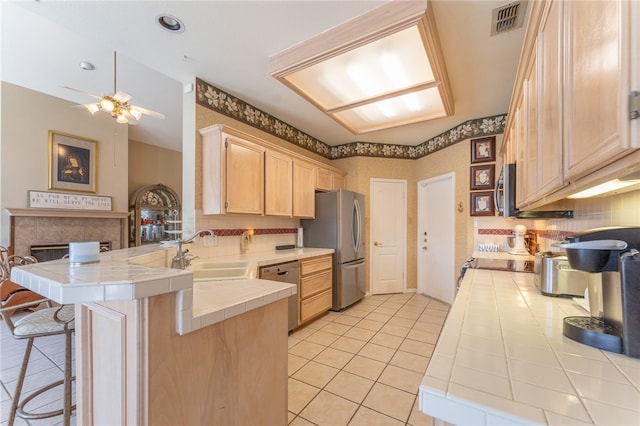 kitchen with tile counters, kitchen peninsula, appliances with stainless steel finishes, and sink