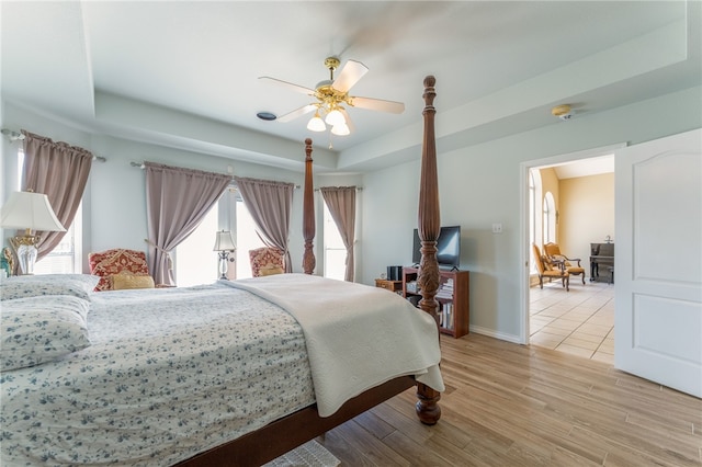 bedroom with multiple windows, light hardwood / wood-style floors, ceiling fan, and a tray ceiling