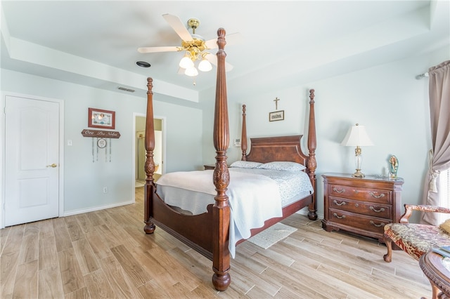 bedroom featuring light hardwood / wood-style floors, ceiling fan, and a tray ceiling