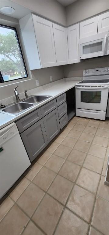 kitchen with light tile patterned floors, white appliances, white cabinetry, and sink