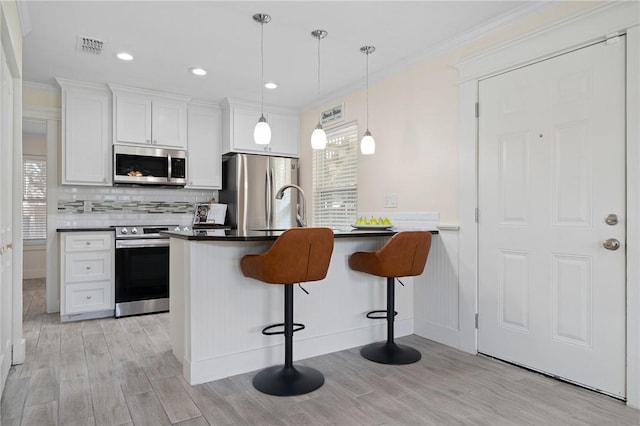 kitchen featuring a breakfast bar area, hanging light fixtures, appliances with stainless steel finishes, light hardwood / wood-style floors, and white cabinets