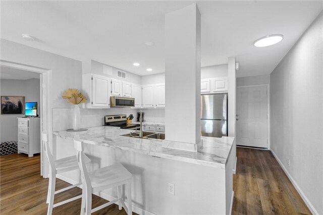 kitchen with stainless steel appliances, sink, kitchen peninsula, dark hardwood / wood-style floors, and white cabinets