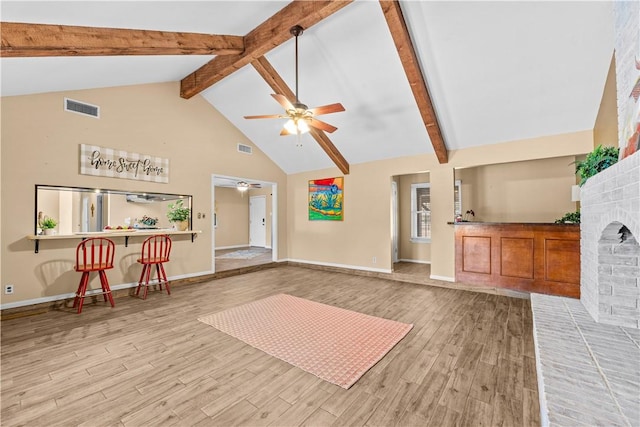 interior space featuring light wood-type flooring, visible vents, beamed ceiling, a brick fireplace, and ceiling fan