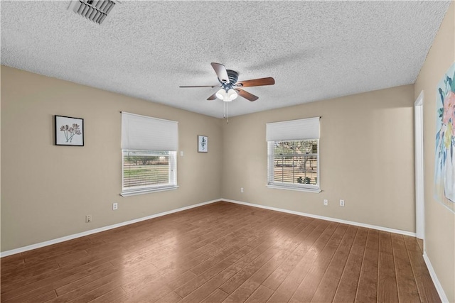 empty room with visible vents, a textured ceiling, wood finished floors, baseboards, and ceiling fan
