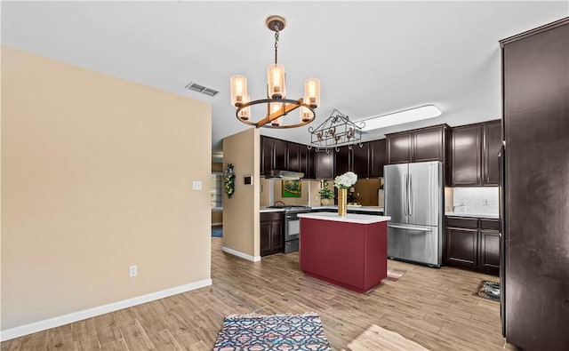 kitchen featuring visible vents, a center island with sink, light countertops, a notable chandelier, and stainless steel appliances
