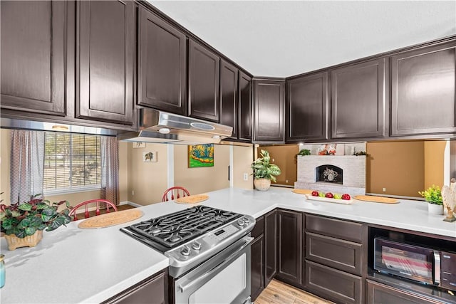 kitchen with stainless steel gas range oven, dark brown cabinets, under cabinet range hood, and light countertops