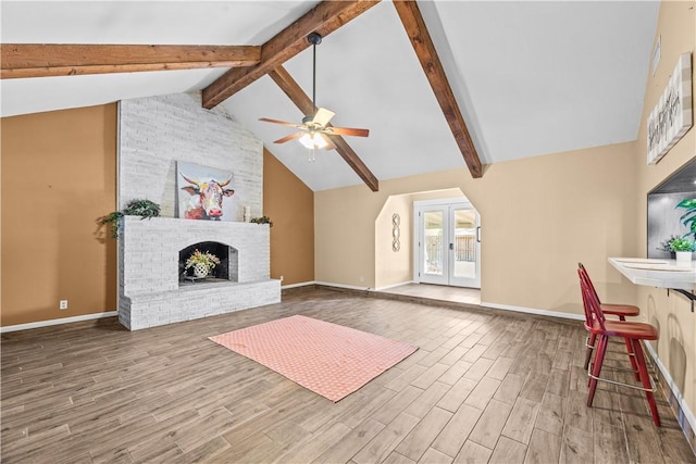 unfurnished living room featuring beamed ceiling, a ceiling fan, wood finished floors, baseboards, and a brick fireplace