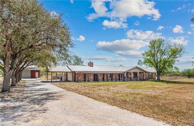 single story home featuring a front lawn, a chimney, metal roof, driveway, and a standing seam roof
