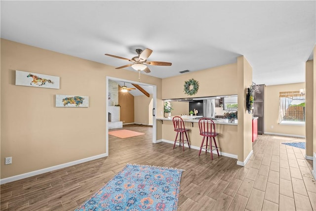 kitchen with freestanding refrigerator, a kitchen bar, a ceiling fan, and wood finished floors