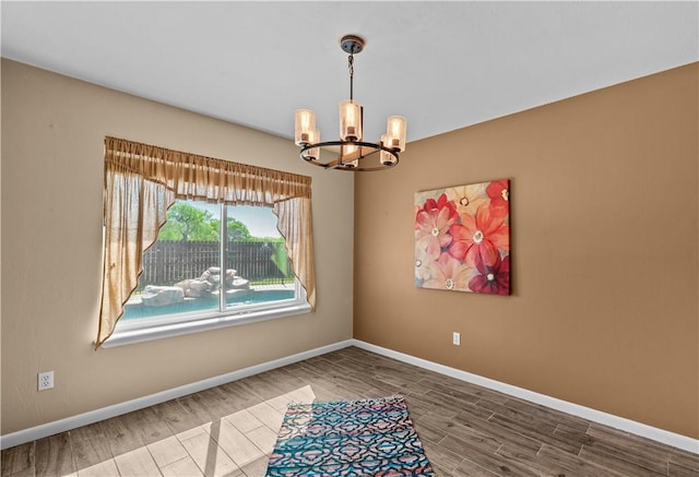 empty room featuring a chandelier, baseboards, and wood finished floors