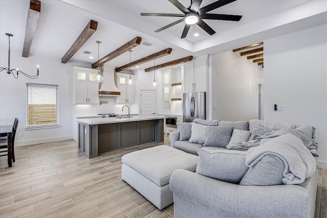 living room with ceiling fan with notable chandelier, beam ceiling, and sink