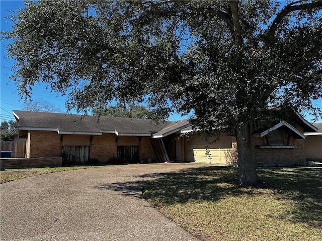 ranch-style home featuring driveway, a garage, brick siding, roof with shingles, and a front yard