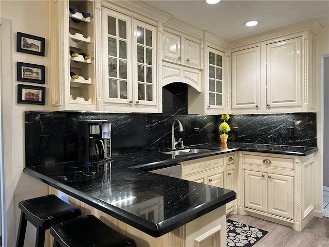 kitchen featuring a peninsula, light wood-style flooring, a sink, and glass insert cabinets