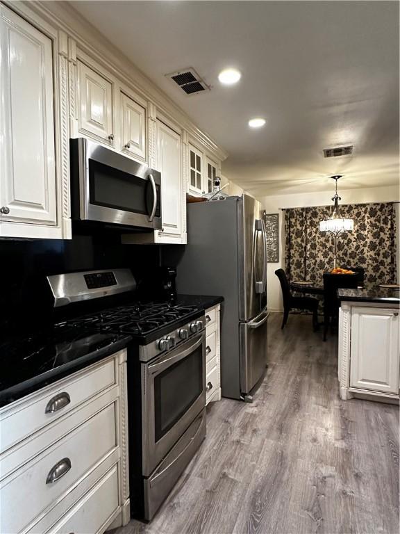 kitchen with visible vents, dark countertops, appliances with stainless steel finishes, glass insert cabinets, and hanging light fixtures