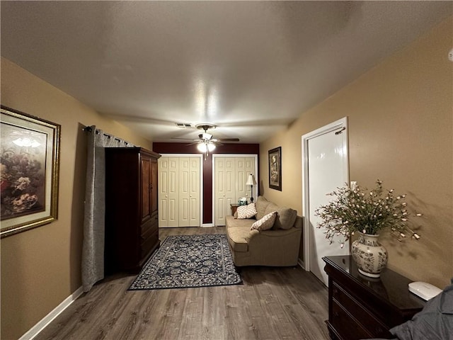 living area with ceiling fan, visible vents, baseboards, and dark wood-style flooring