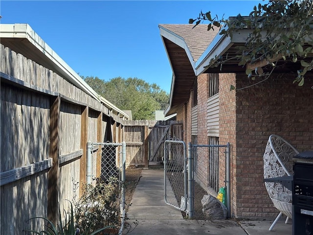 view of property exterior featuring brick siding, a shingled roof, fence, and a gate